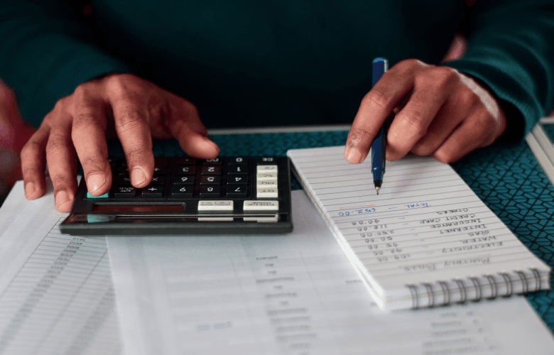 Een man in een groene trui die zijn belastingen, zijn vaste kosten en zijn bijdrage aan de zorgkas en verzekeringen aan het berekenen is met een rekenmachine.