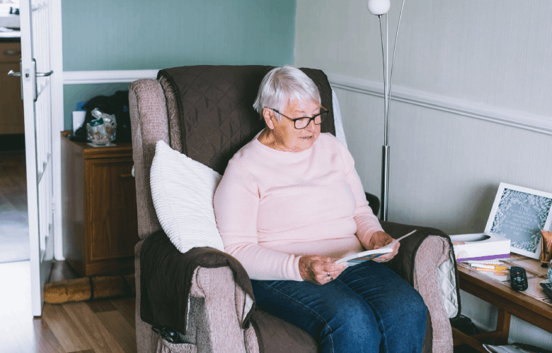 Een oudere vrouw in een zachte fauteuil die een boekje leest.