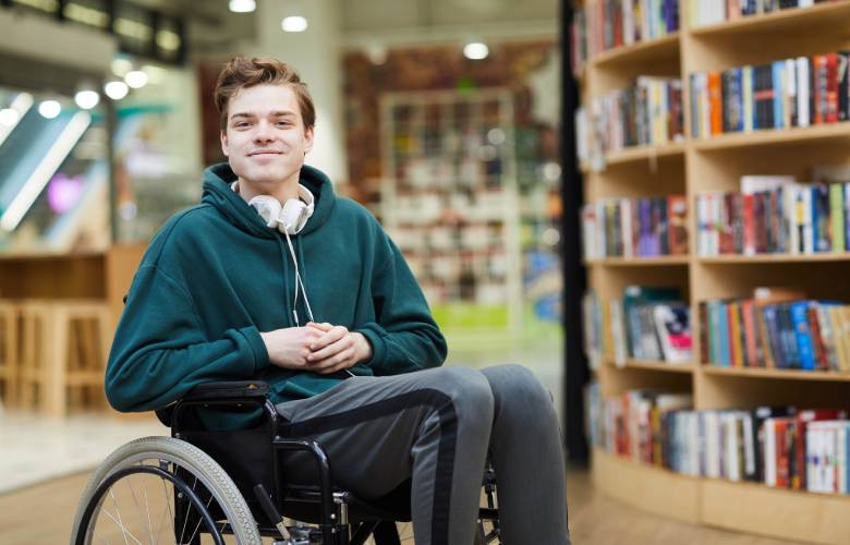 Jongen met beperking in een rolstoel in een bibliotheek.