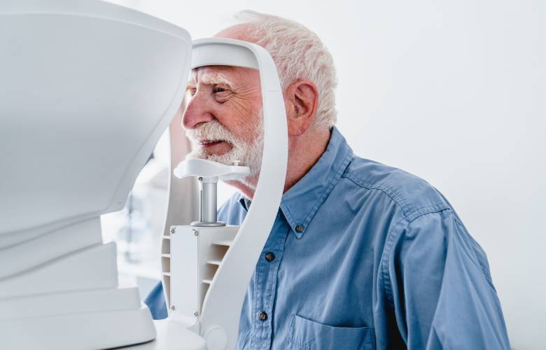 Een oudere man controleert zijn ogen op cataract zodat hij een terugbetaling kan krijgen van zijn ziekenfonds.