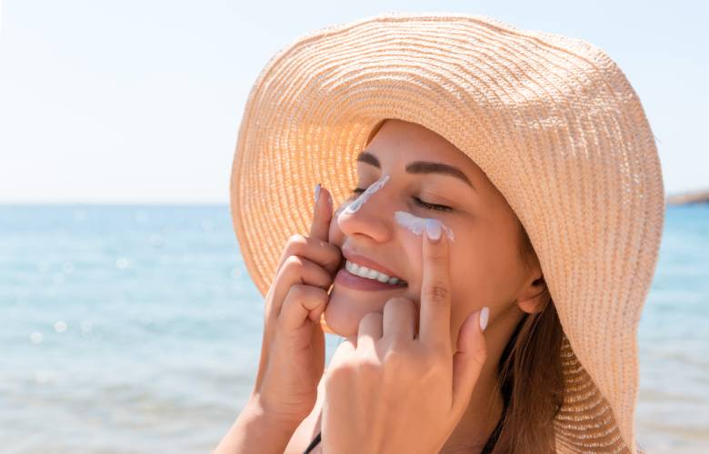 Vrouw smeert zonnecrème op haar gezicht.