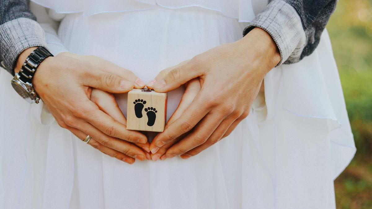 Koppel vormt een hartje rond de zwangere buik met een houten blokje met babyvoetjes